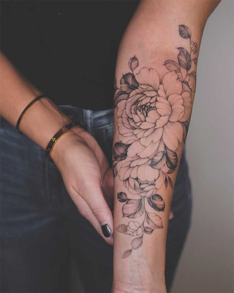 A close-up photo of a colorful floral tattoo on the left inner forearm of a person with light skin.