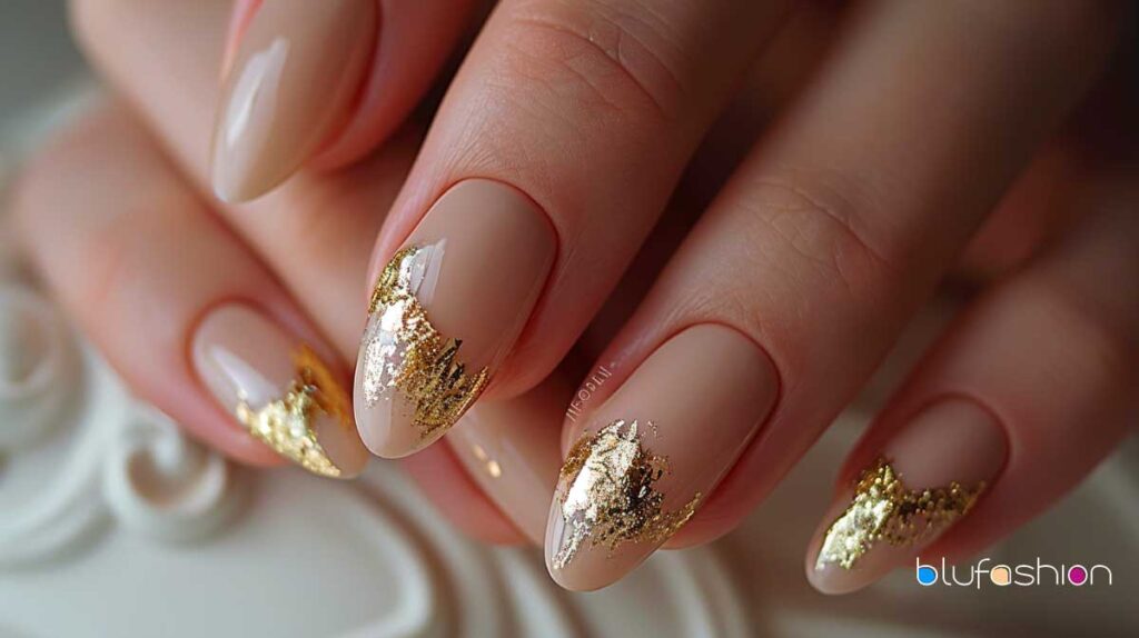 Natural oval nails with chic beige polish and elegant gold leaf accents.