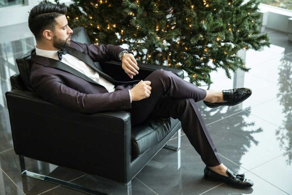 Man in elegant dark purple suit sitting confidently in a modern office lobby with a Christmas tree.