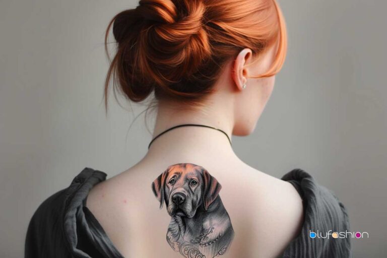 A woman with a redhead bun reveals a detailed black and grey tattoo of a dog on her upper back, with ornamental design elements.