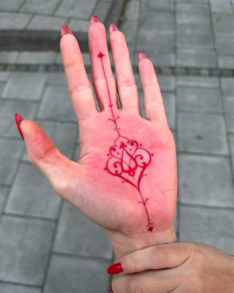 A red tattoo of a dragon on the palm of a person's hand.