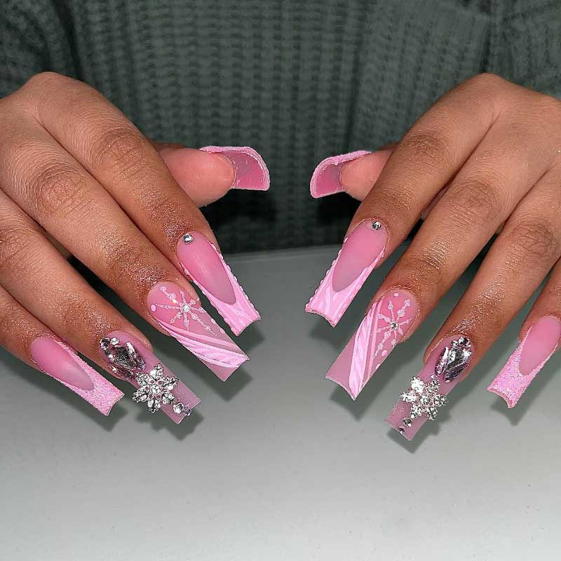 Pink winter nails with frosted tips, delicate snowflake art, and shiny crystal embellishments.