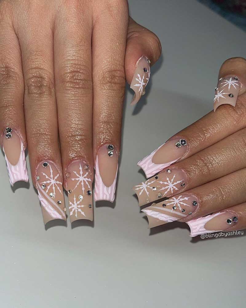 Long almond-shaped nails with pale pink base, white snowflake design, and sparkling rhinestone accents for a winter look.