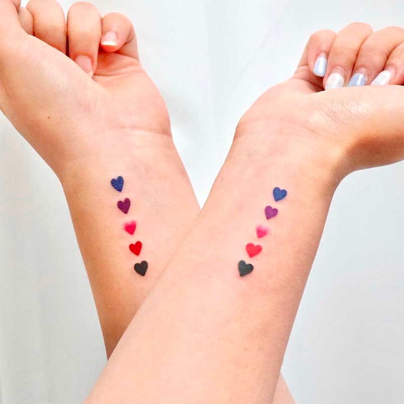 A young woman holding hands with matching heart tattoos on their wrists.