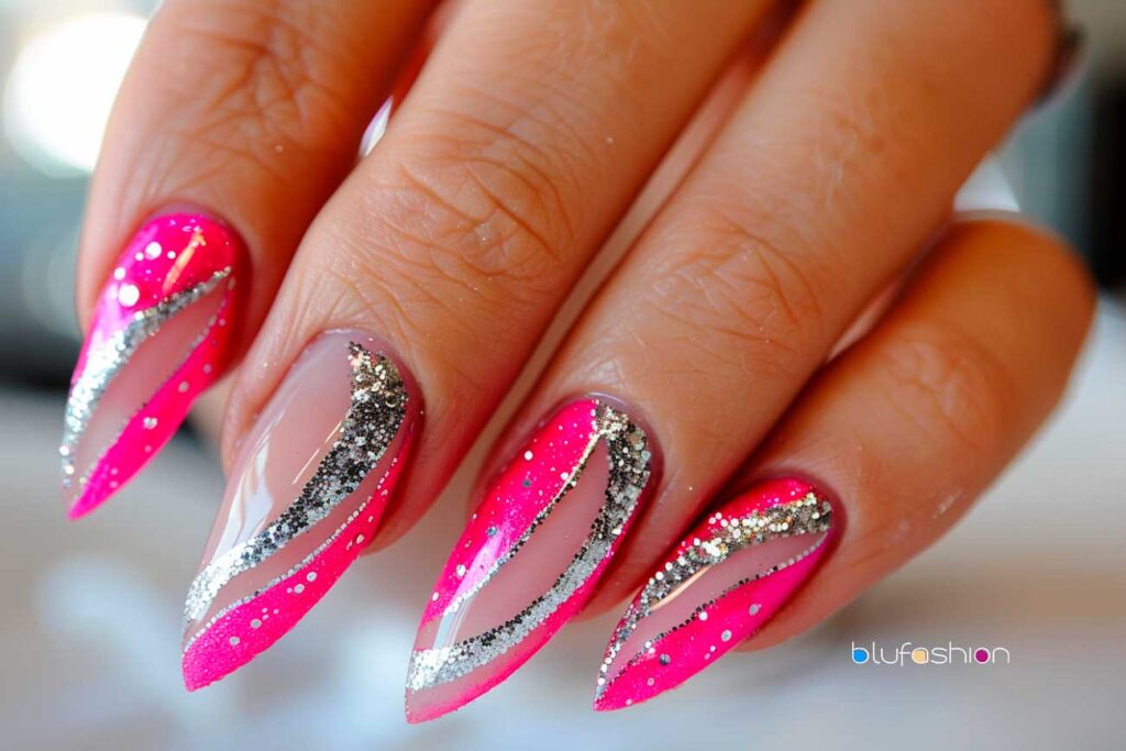 Stiletto nails painted in a vivid hot pink hue featuring intricate designs with silver glitter and diamond rhinestone accents for a bold and glamorous look.