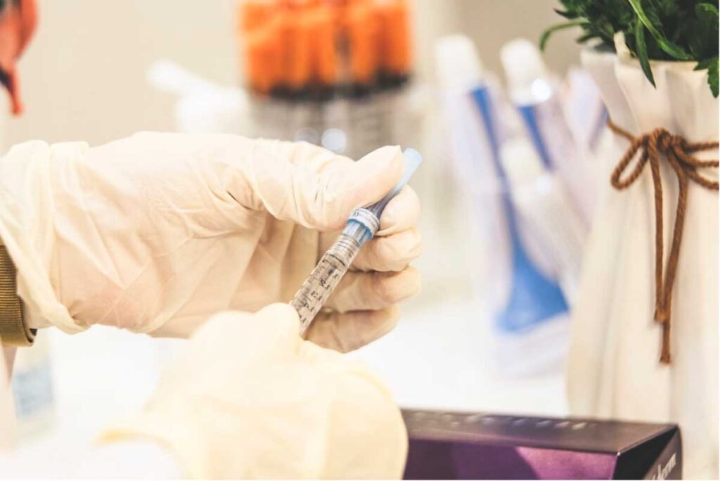 Gloved hand preparing hyaluronic acid injection with blurred beauty products background.