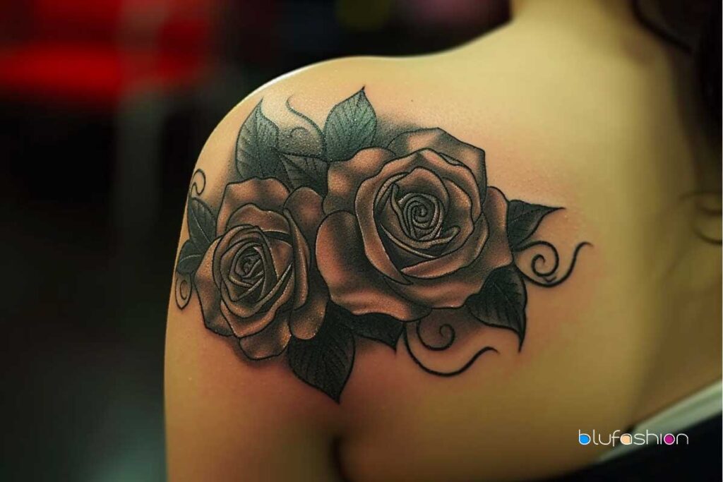 Twin roses with intricate black shading and elegant swirl accents on a curving shoulder.