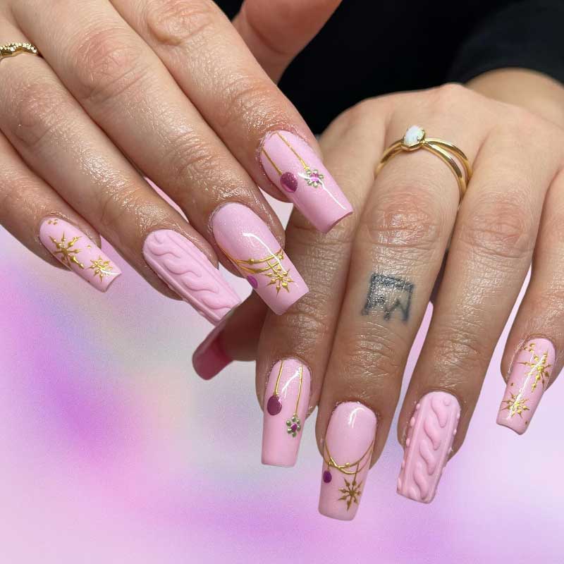 Pastel pink coffin nails with gold accents, cable knit textures, and floral nail art.