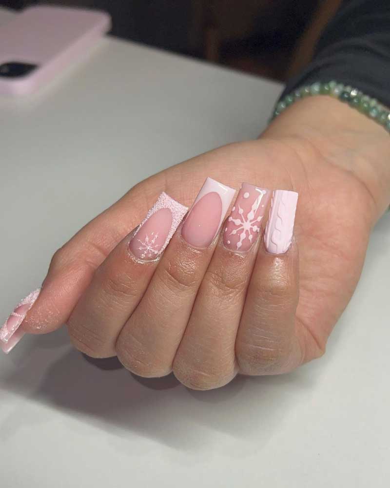 Elegant hand displaying winter-inspired nail art with glossy pink and white polish, featuring snowflake and sweater designs.