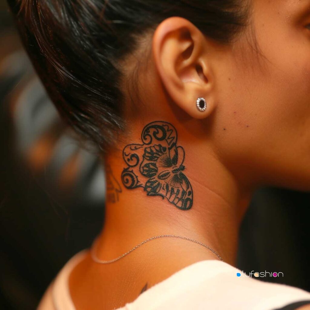 Small intricate butterfly skull tattoo on woman's neck with stud earring.