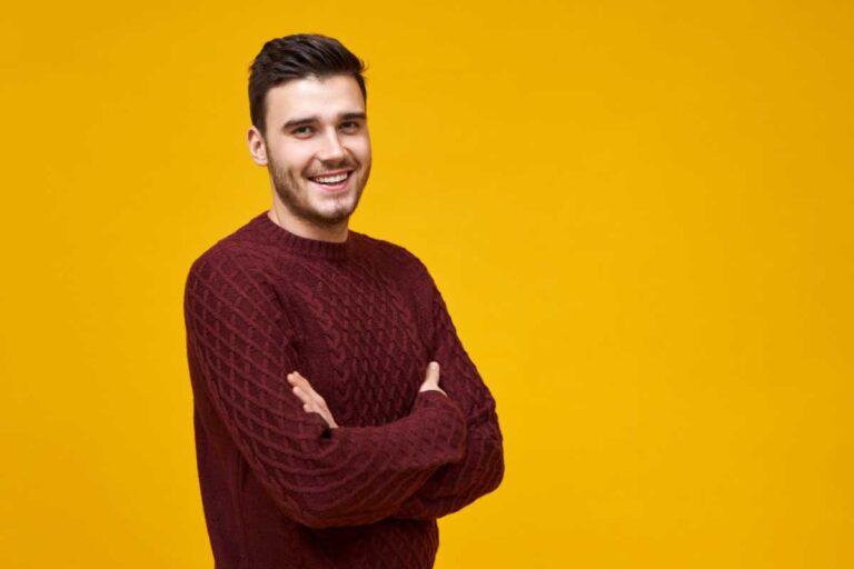 Cheerful man with crossed arms wearing a maroon sweater on a yellow background.