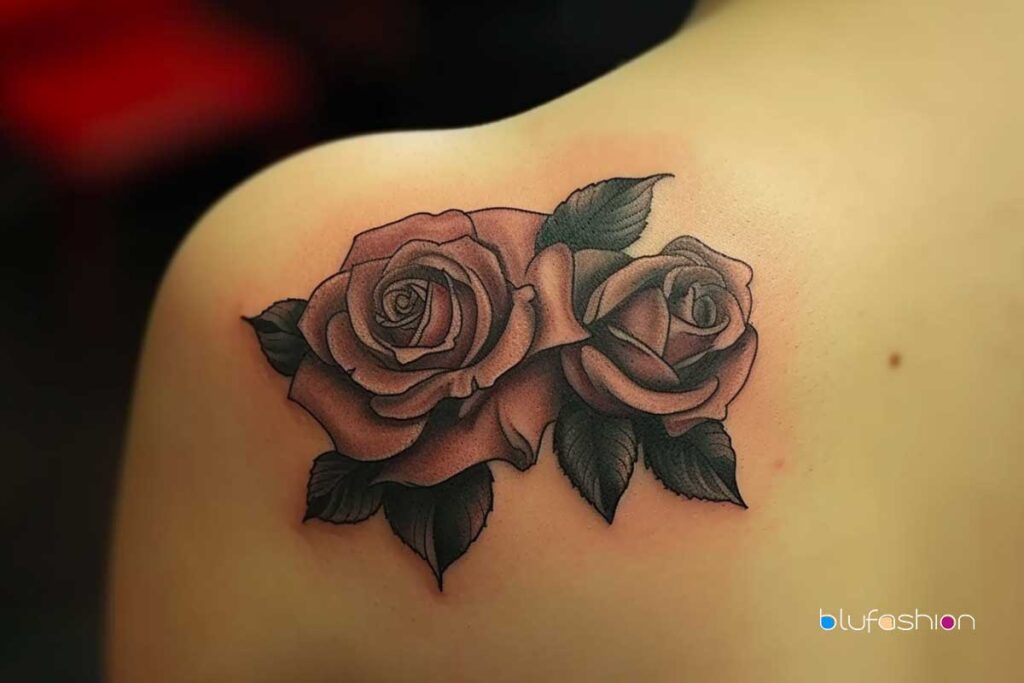 Pair of rose tattoos with soft pink shading and dark leaves on a smooth shoulder.