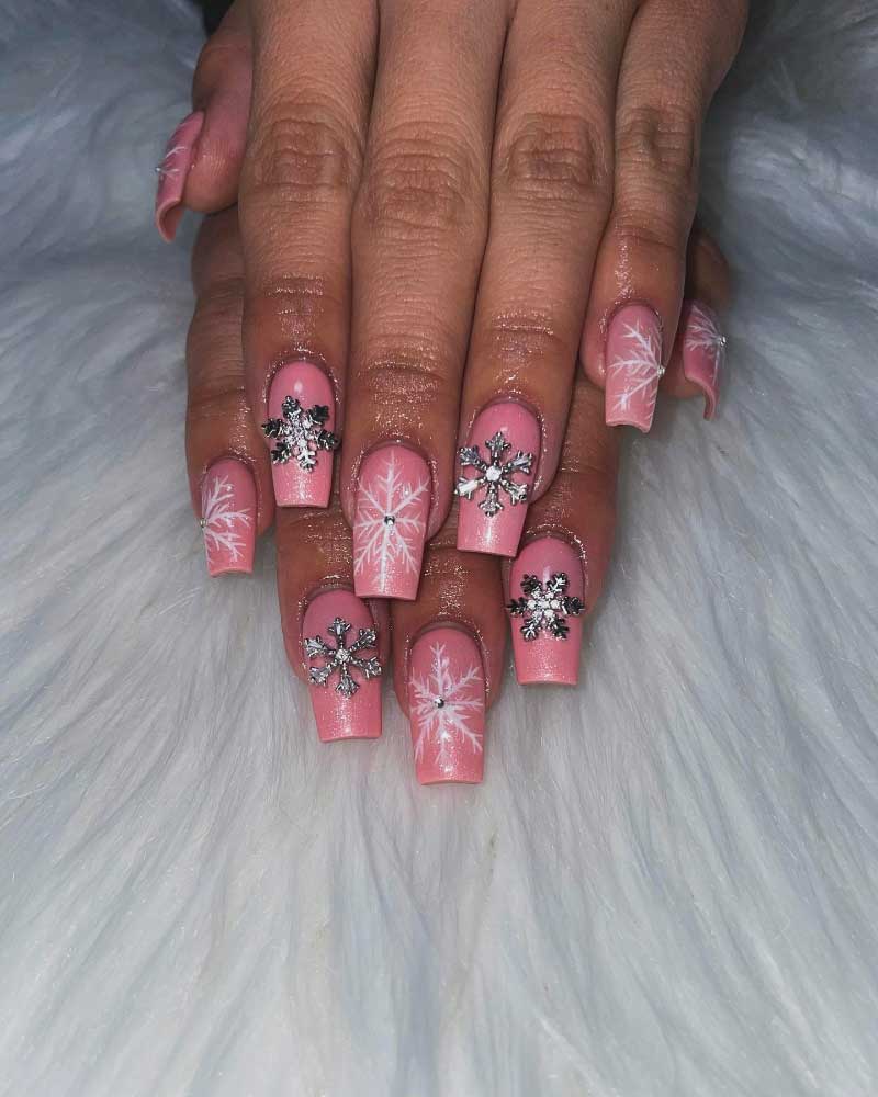 Baby pink square nails with white snowflake patterns and silver snowflake jewels on plush background.